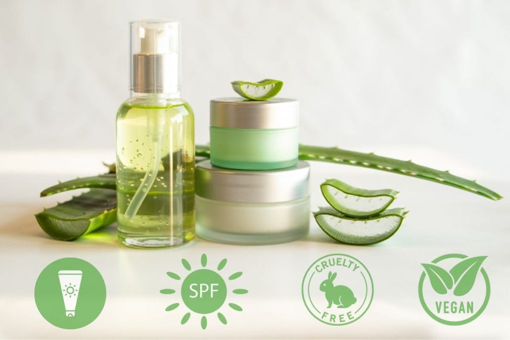 Hudvårdsprodukter med aloe vera i glasflaska och burkar, omgivna av aloe vera-blad och symboler för SPF, cruelty-free och vegan.