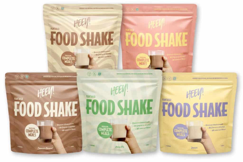 Fem olika förpackningar av Heey! Food Shake i olika färger och smaker, uppställda tillsammans. Varje påse visar ett glas shake som hålls upp av en hand.